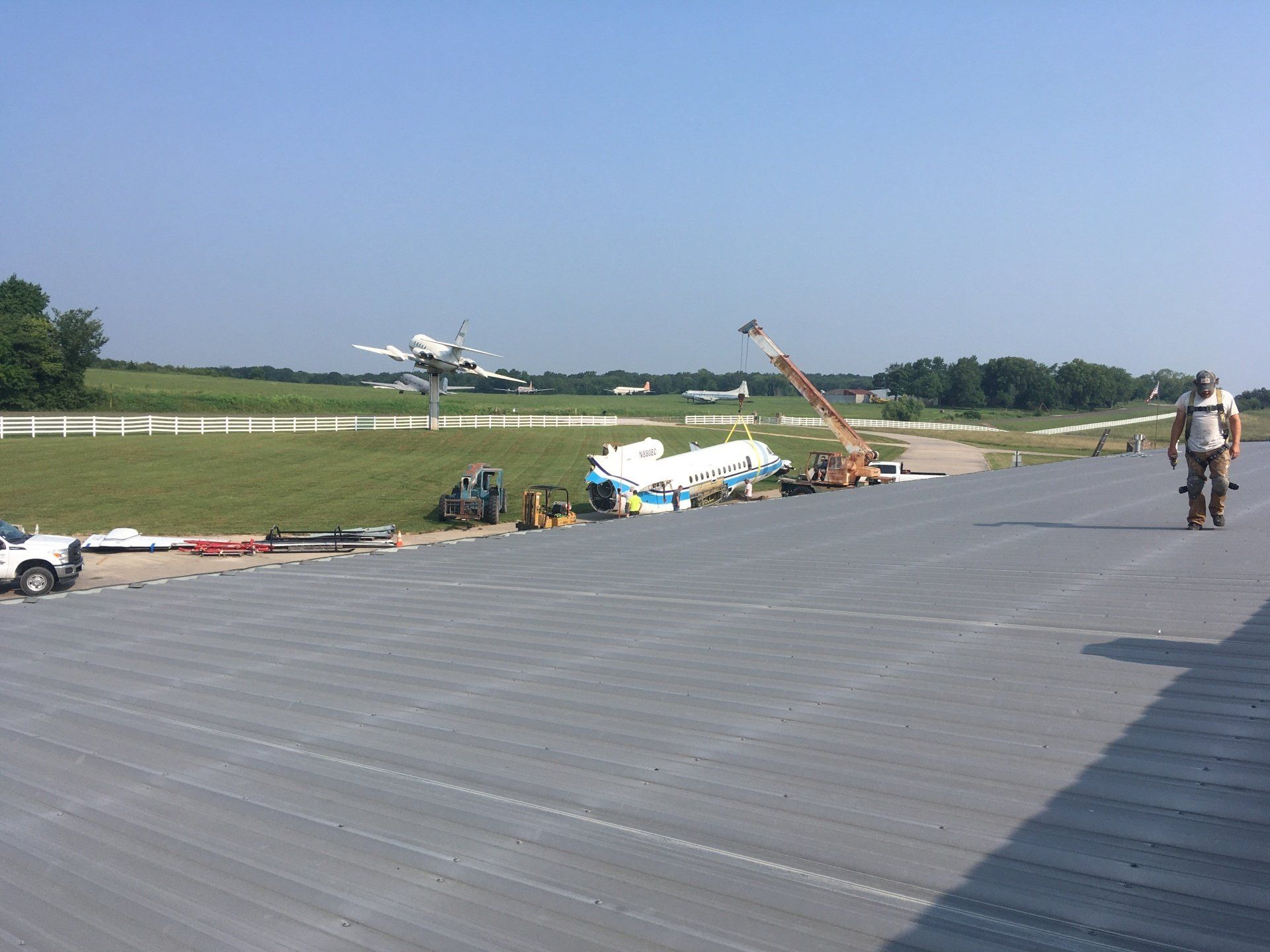 A man is walking on a metal roof with a plane and runway in the background.