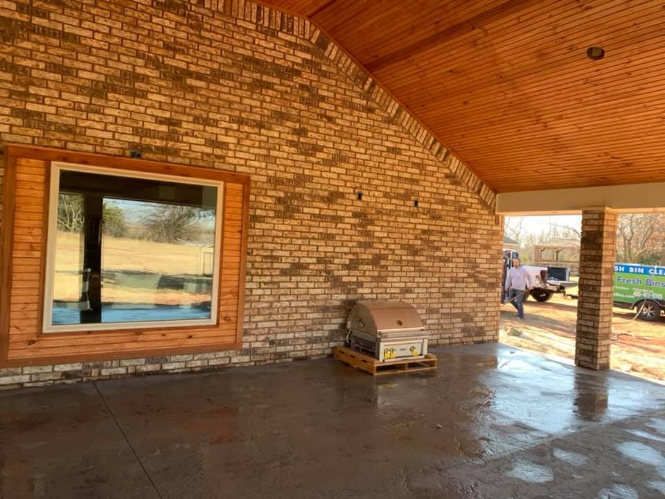 Covered brick patio with arched ceiling, large window, and grill near the wall.