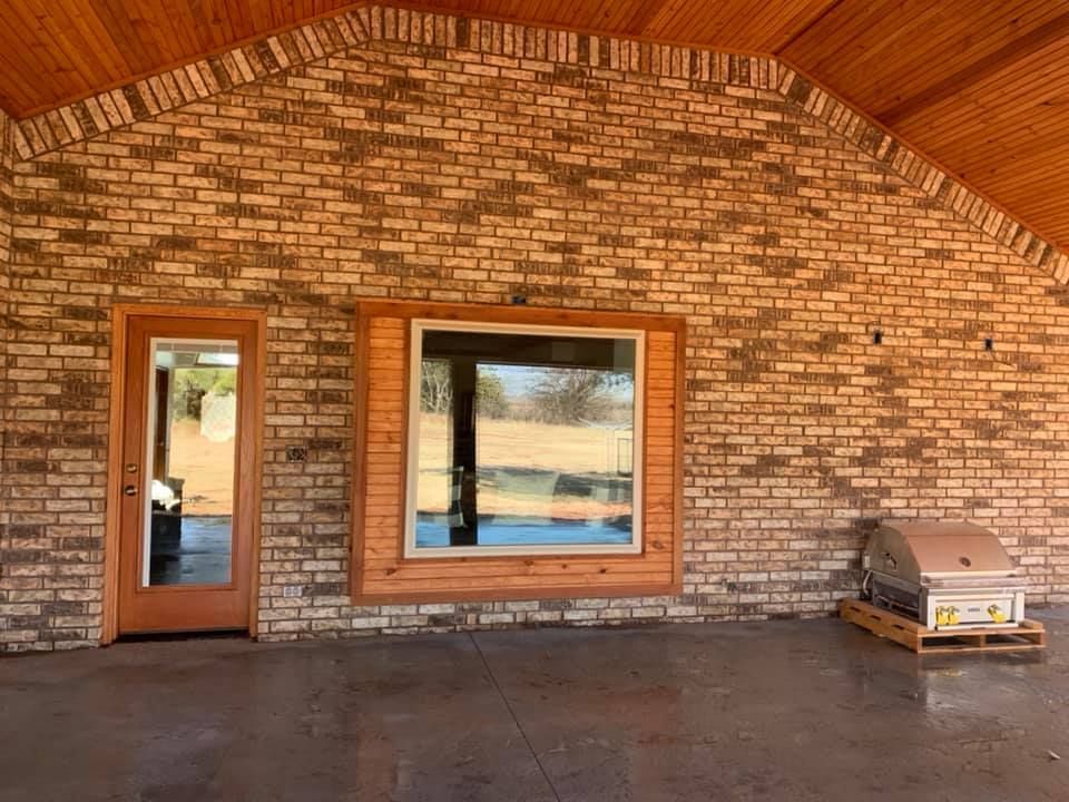 Brick porch under a wood ceiling with a window, door, and a small bench on the right.