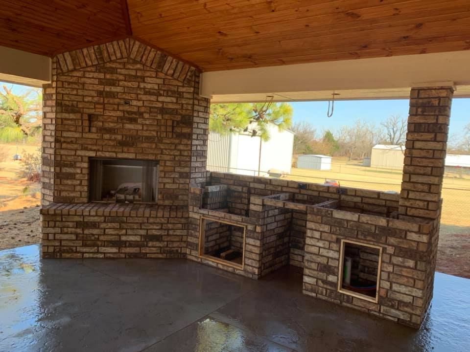 Brick outdoor patio with covered roof, fireplace, and built-in grill under an open view of the yard