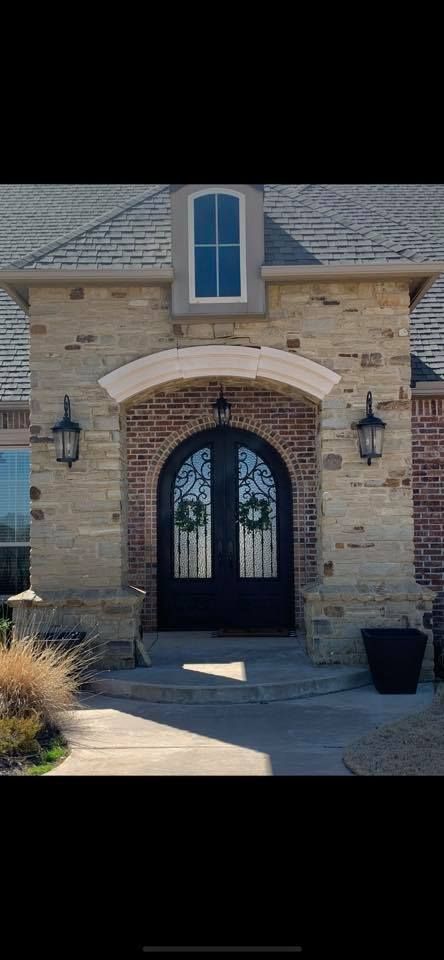 Front entrance of a brick house with an arched doorway, wrought-iron gate, and lanterns flanking the door