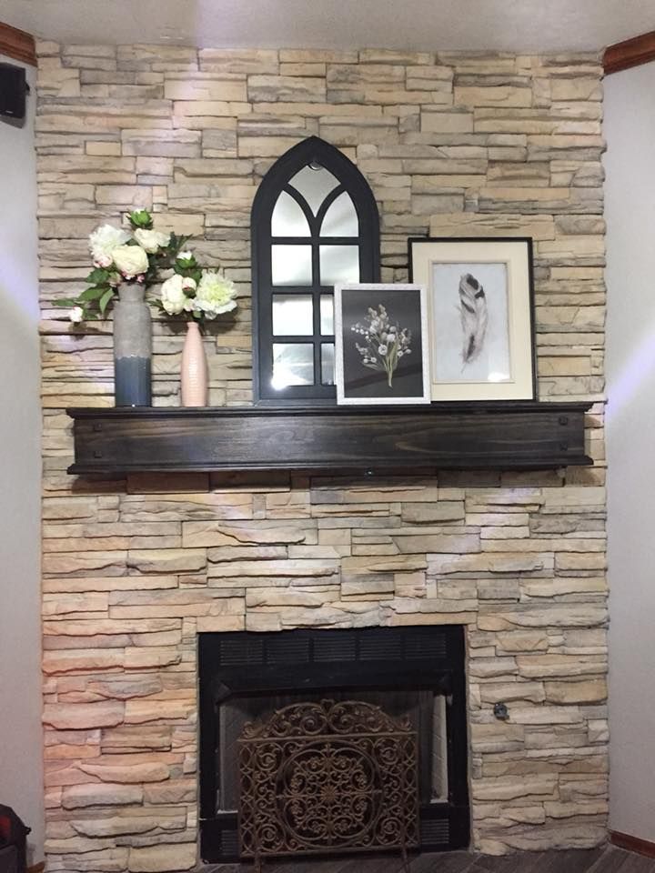 Stone fireplace with dark mantel, arched mirror, framed art, and vase of white flowers.