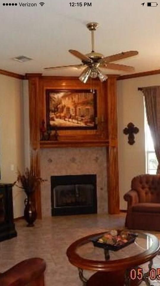 Cozy living room with fireplace, ceiling fan, framed art, curtains, and leather chair by a glass coffee table.