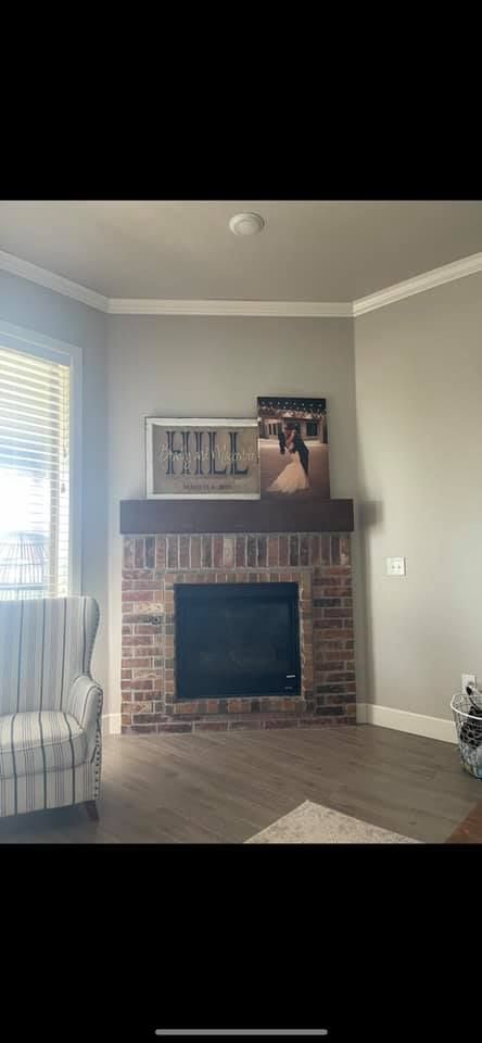 Living room corner with brick fireplace, framed art, and a window with blinds