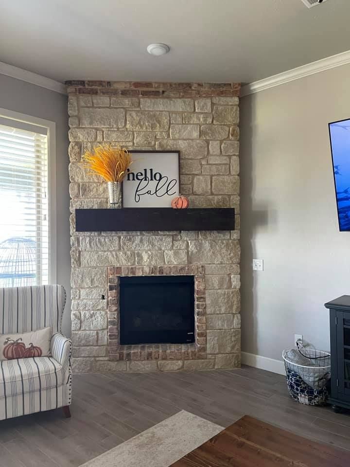Stone fireplace with dark mantel, fall decor, and TV in a cozy living room