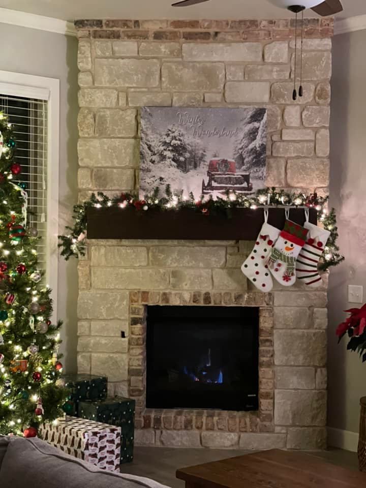 Cozy stone fireplace decorated with Christmas garland, stockings, and a snowy village painting above the mantel