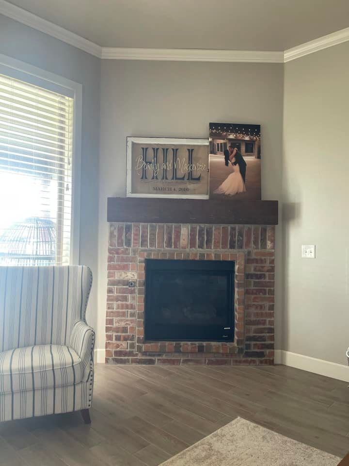 Living room corner with brick fireplace, framed art, striped chair, and window blinds