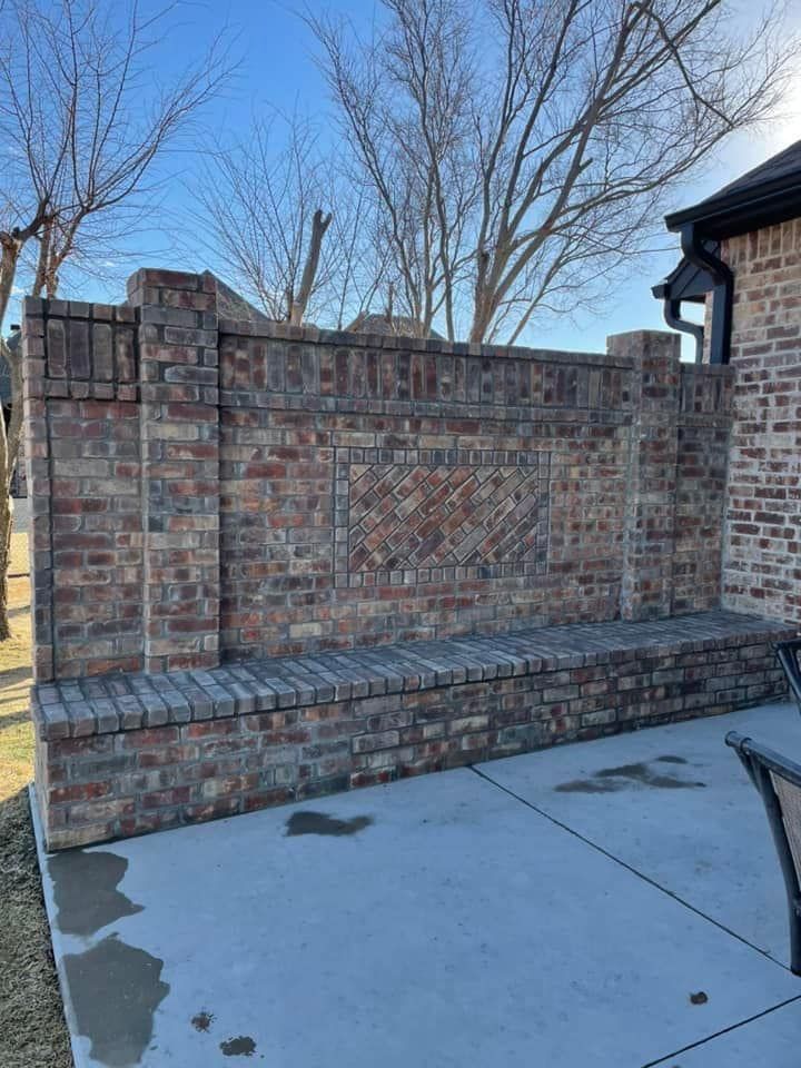 Brick outdoor fireplace and built-in bench beside a concrete patio in a backyard.
