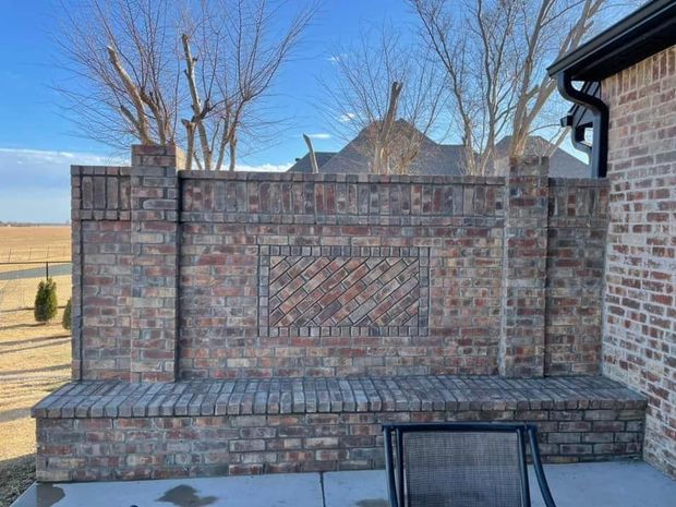 Brick outdoor bench and low wall in a yard with bare trees and blue sky.