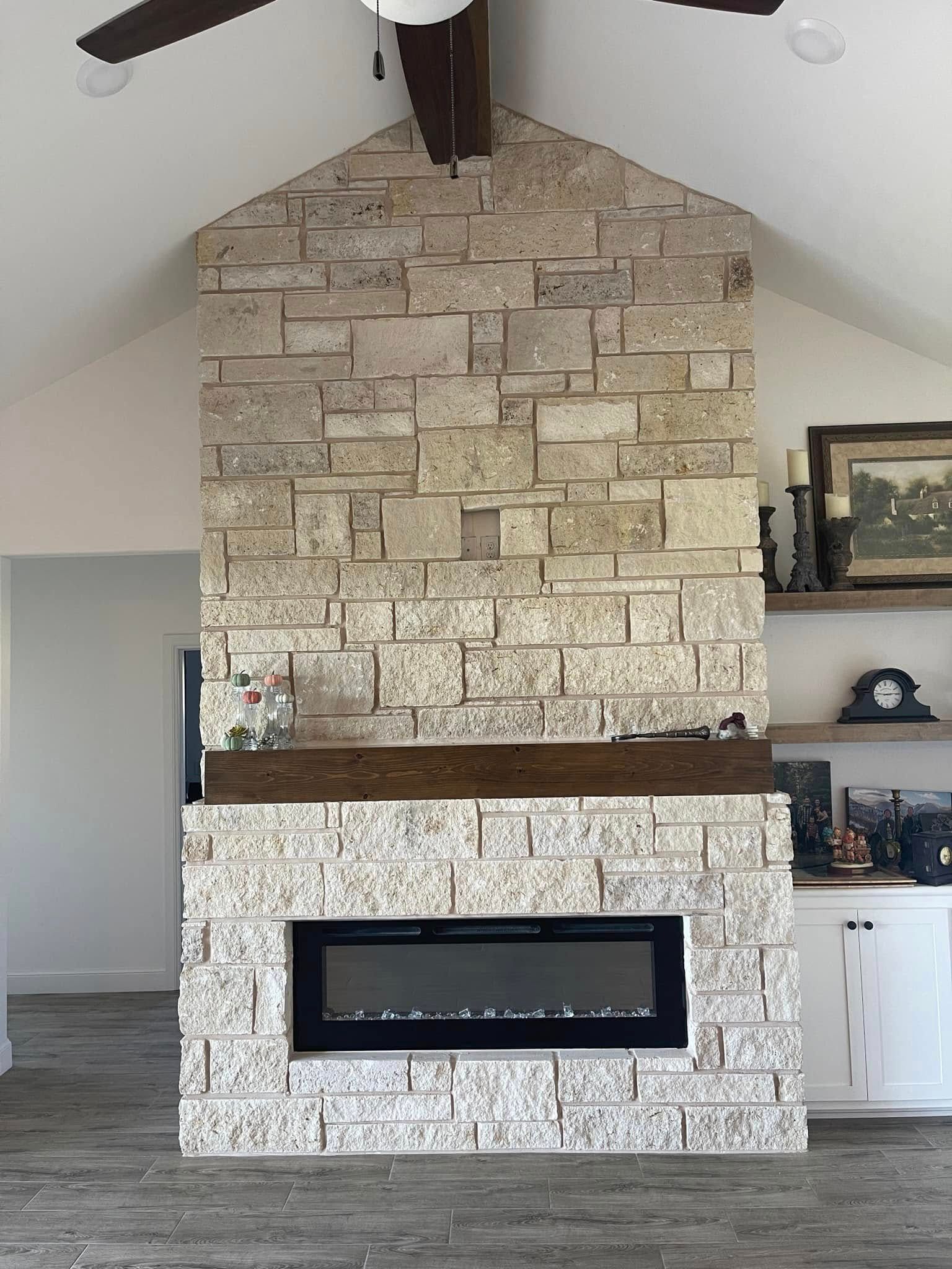 Stone fireplace with a black electric insert in a bright living room with shelves and ceiling fan.