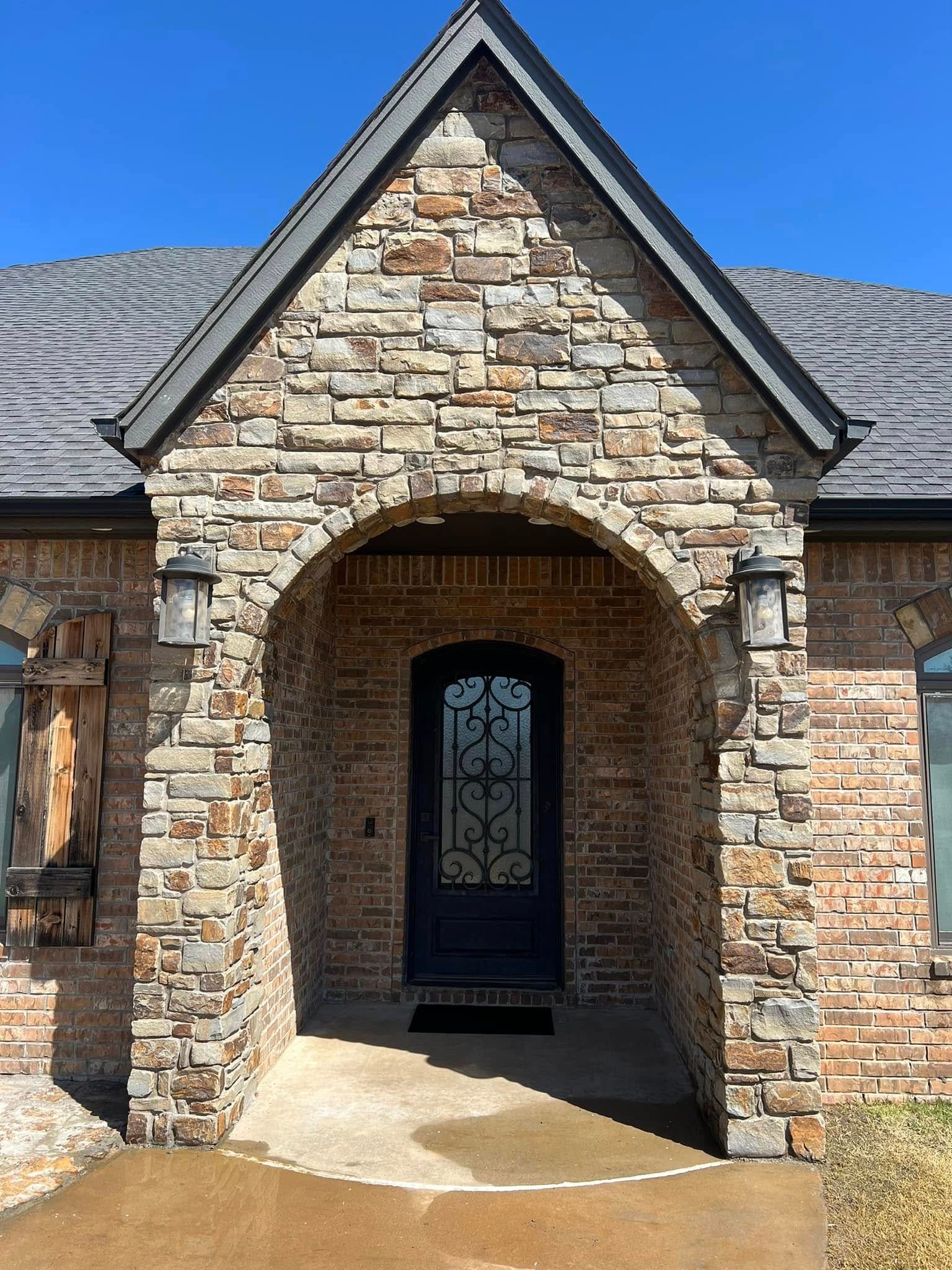Stone house entrance with arched porch and black front door under a peaked roof.