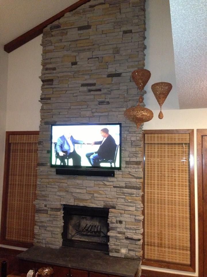 Stone fireplace with a wall-mounted TV, wicker side panels, and decorative wall hangings in a living room.