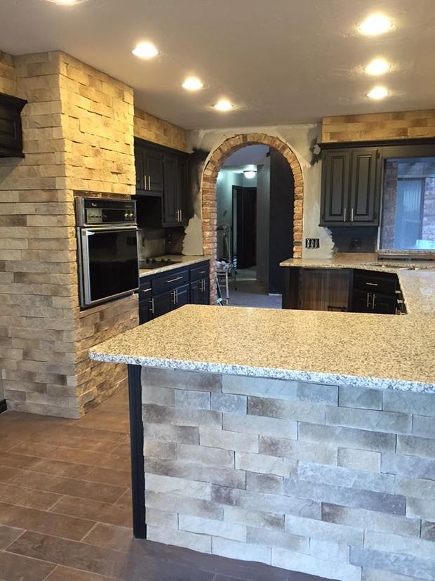 Modern kitchen with stone accents, granite island, dark cabinets, and recessed ceiling lights.