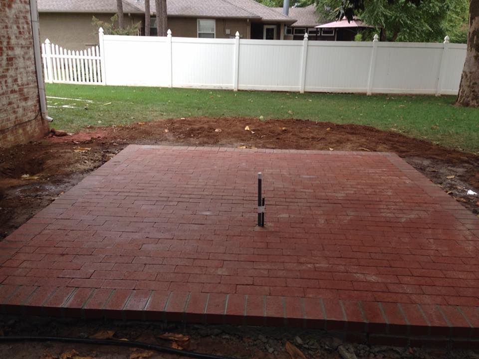 Brick patio in a backyard with a white fence and grassy lawn in the background