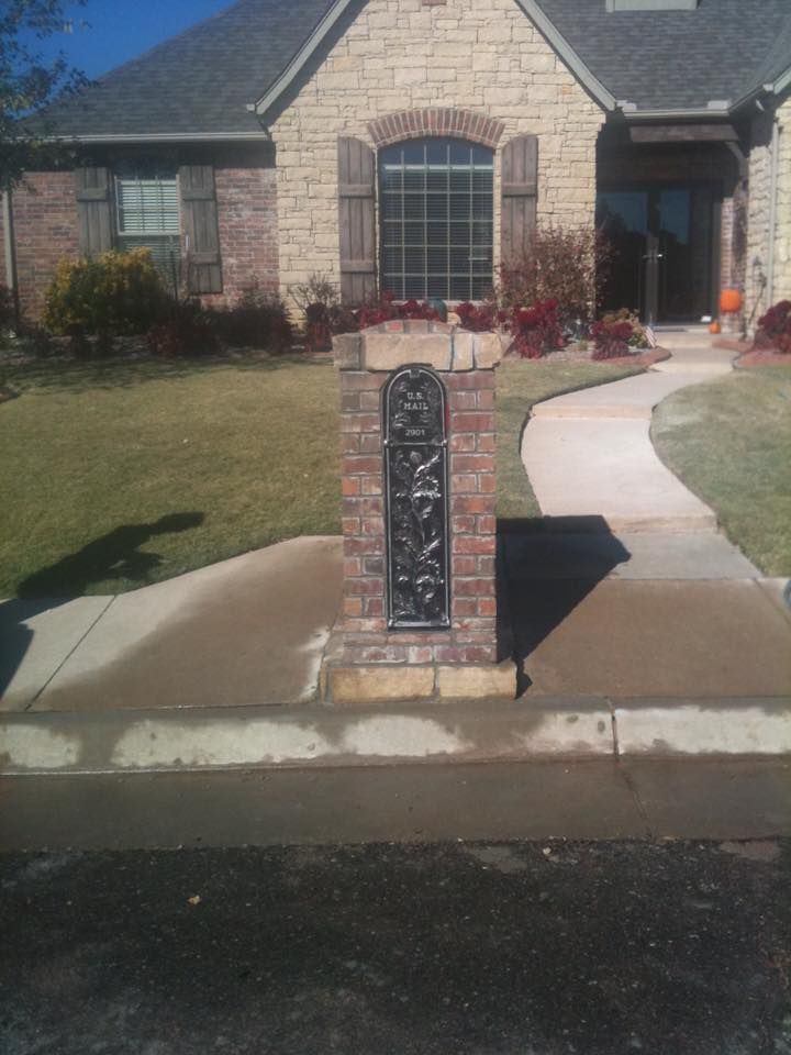Brick mailbox with decorative metal panel beside a curved driveway in front of a suburban house