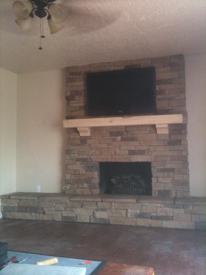Living room with a brick fireplace, mounted TV, and ceiling fan above a stone hearth.