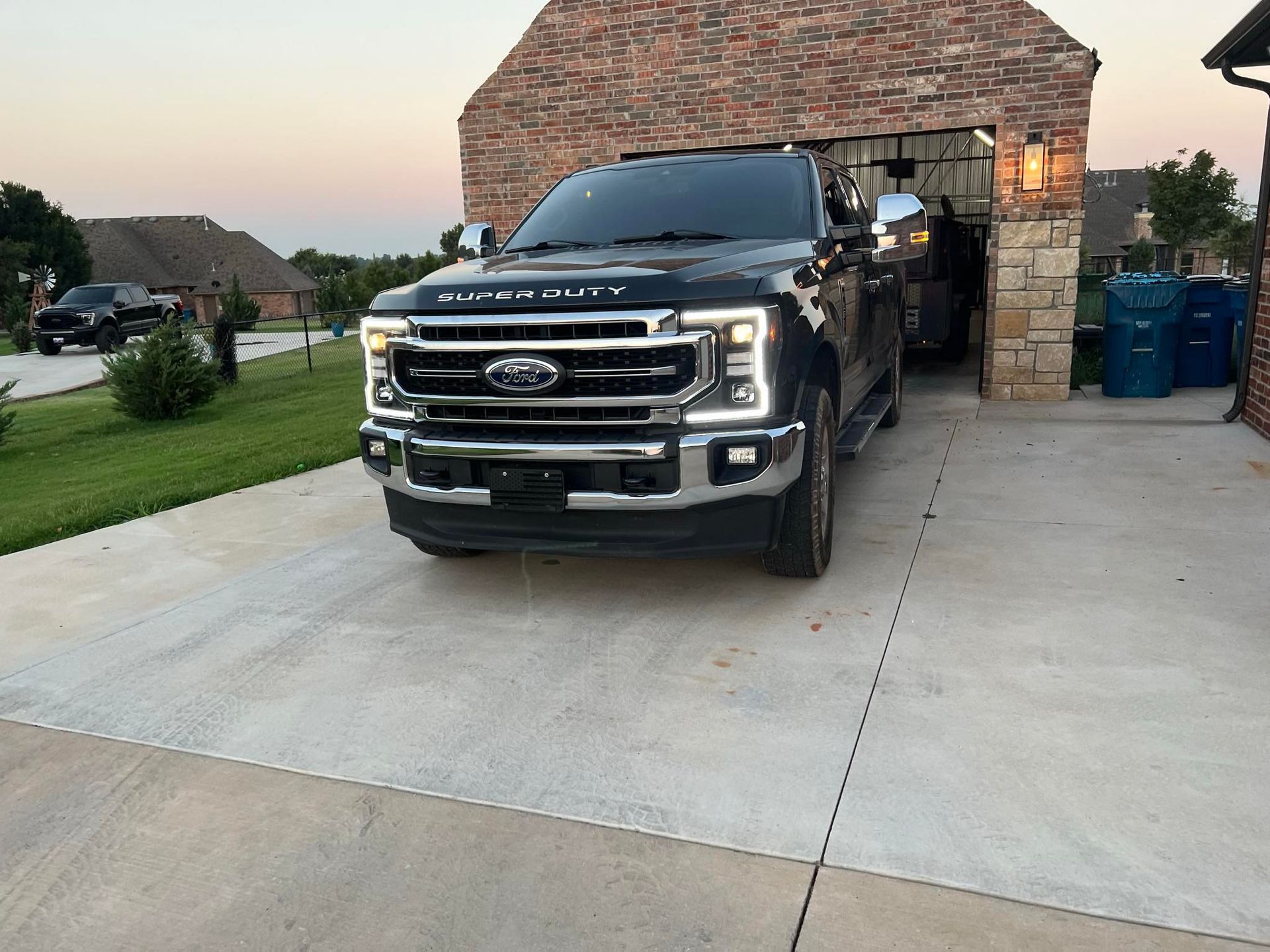 Black Ford pickup parked in a driveway beside a brick garage at dusk