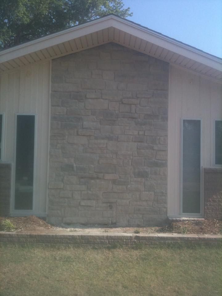 Front view of a small house with a stone center facade, white siding, and narrow windows.