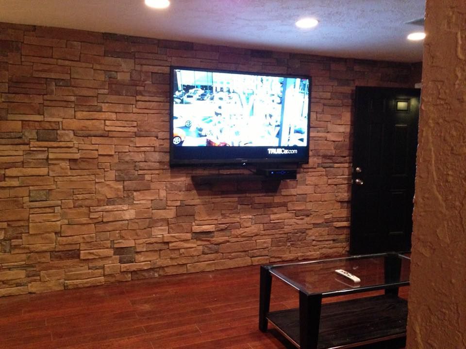 Wall-mounted TV on a stone accent wall in a lounge with wood floor and glass coffee table.
