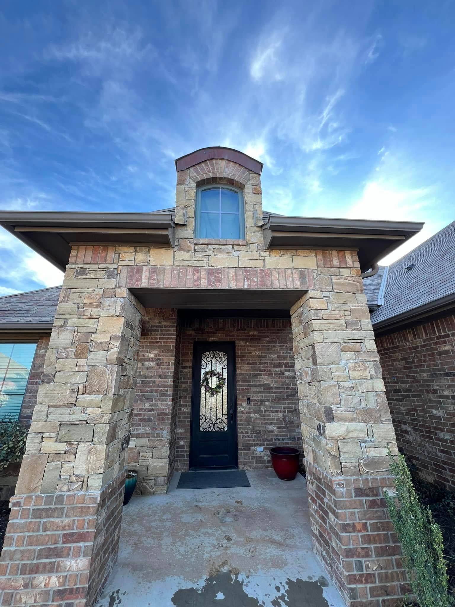 Stone front entry with arched doorway and window, framed by brick and lit by a blue sky.