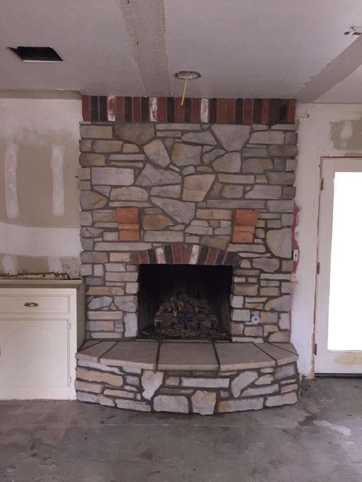 Stone fireplace with a raised hearth in an unfinished room with bare walls and concrete floor