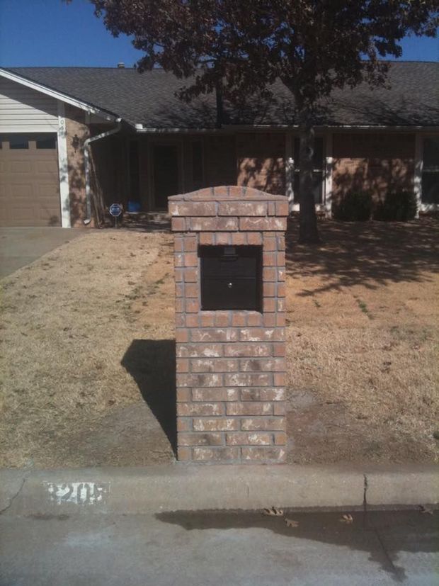 Brick mailbox on a curb in front of a suburban house with a garage.