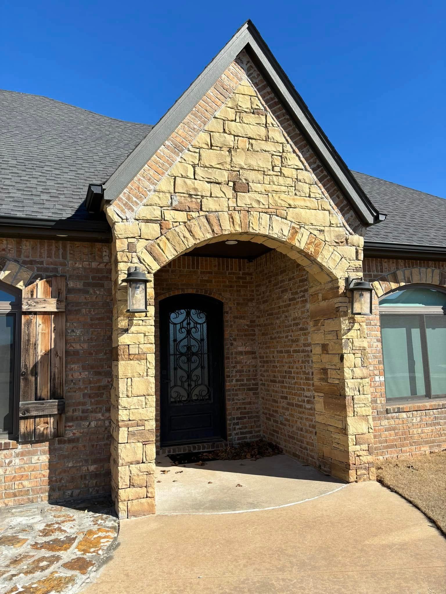 Stone house entrance with arched porch and dark front door under a blue sky