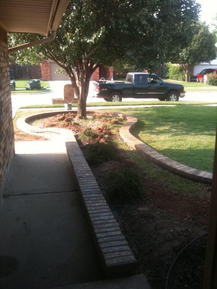 Front porch view of a curved brick walkway, lawn, trees, and a parked pickup truck in a sunny yard