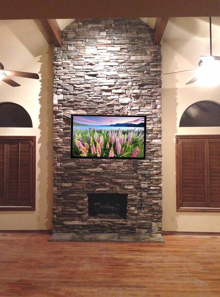 Living room with stone fireplace, mounted TV, wood floor, and shuttered windows