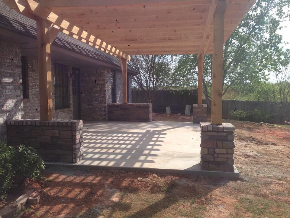 Covered brick patio with wooden pergola, stone columns, and patterned sunlight on the concrete floor