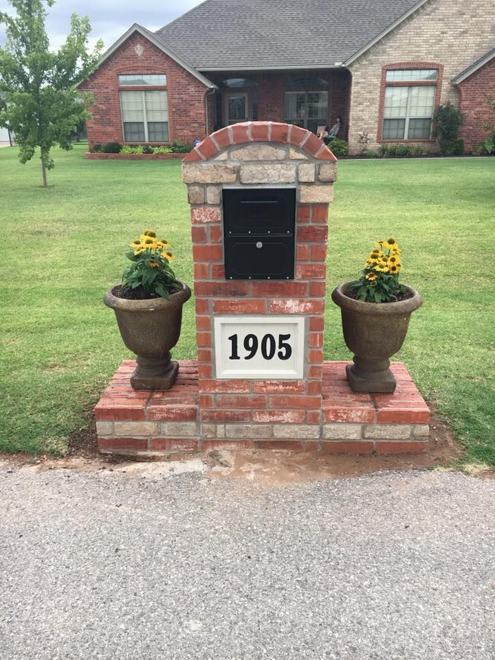 Brick mailbox pillar with black mailbox and flower planters, house number 1905, in front of a suburban home