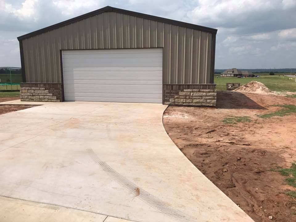 Metal garage with a white roll-up door and concrete driveway in a rural setting