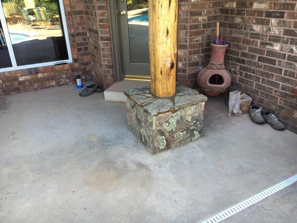 Covered porch with brick wall, concrete floor, wooden post on stone base, and clay chiminea near shoes.