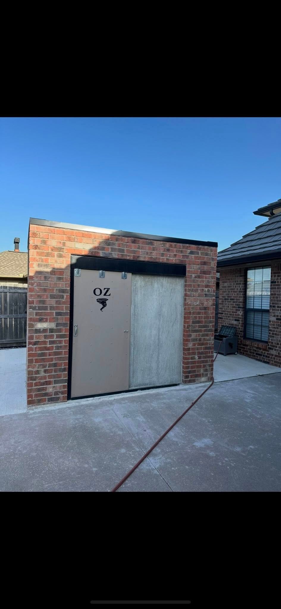 Small brick-and-stucco garage with a gray door on a concrete driveway under a blue sky