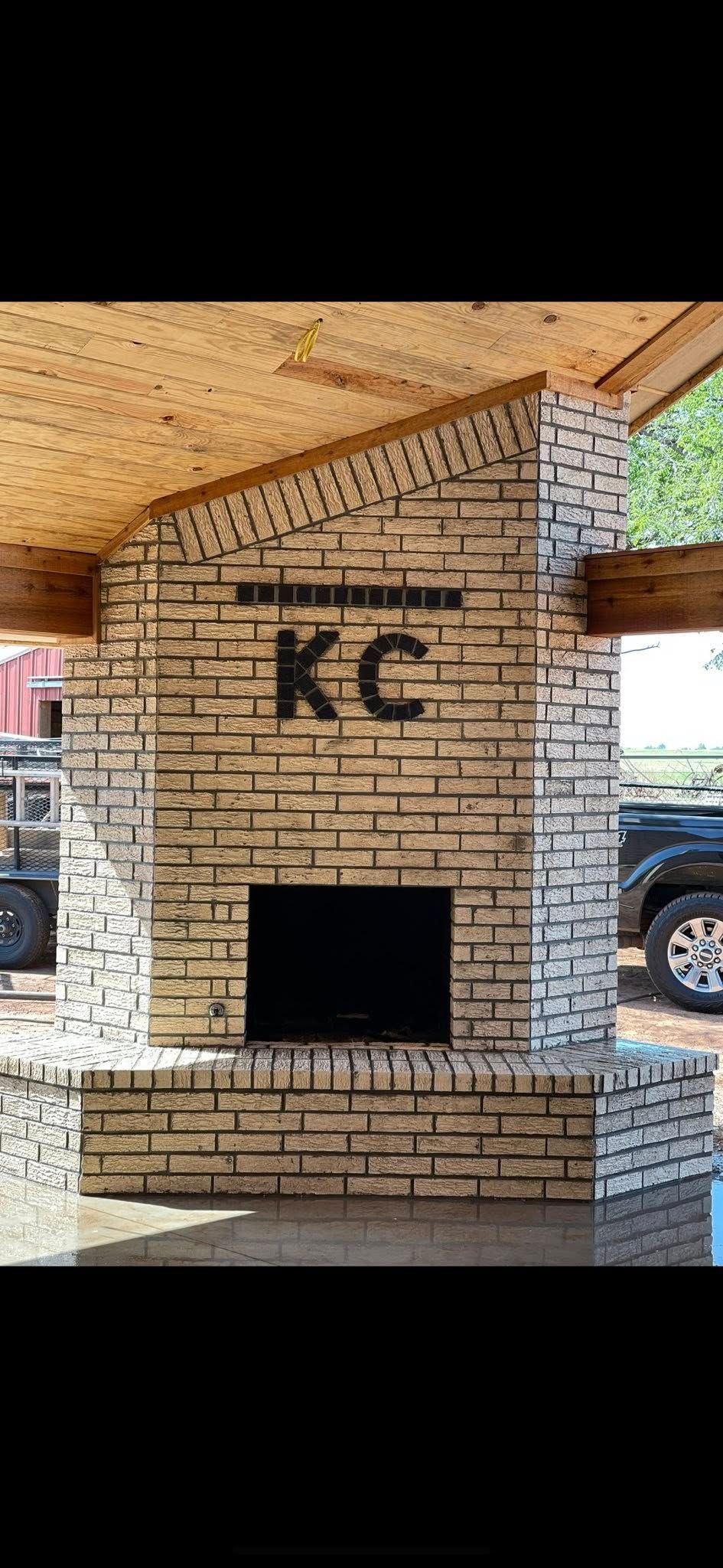 Brick outdoor fireplace with “KC” letters under a covered patio