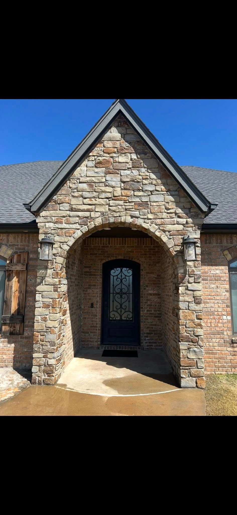 Stone front entrance with arched doorway and gray shingled roof under a blue sky