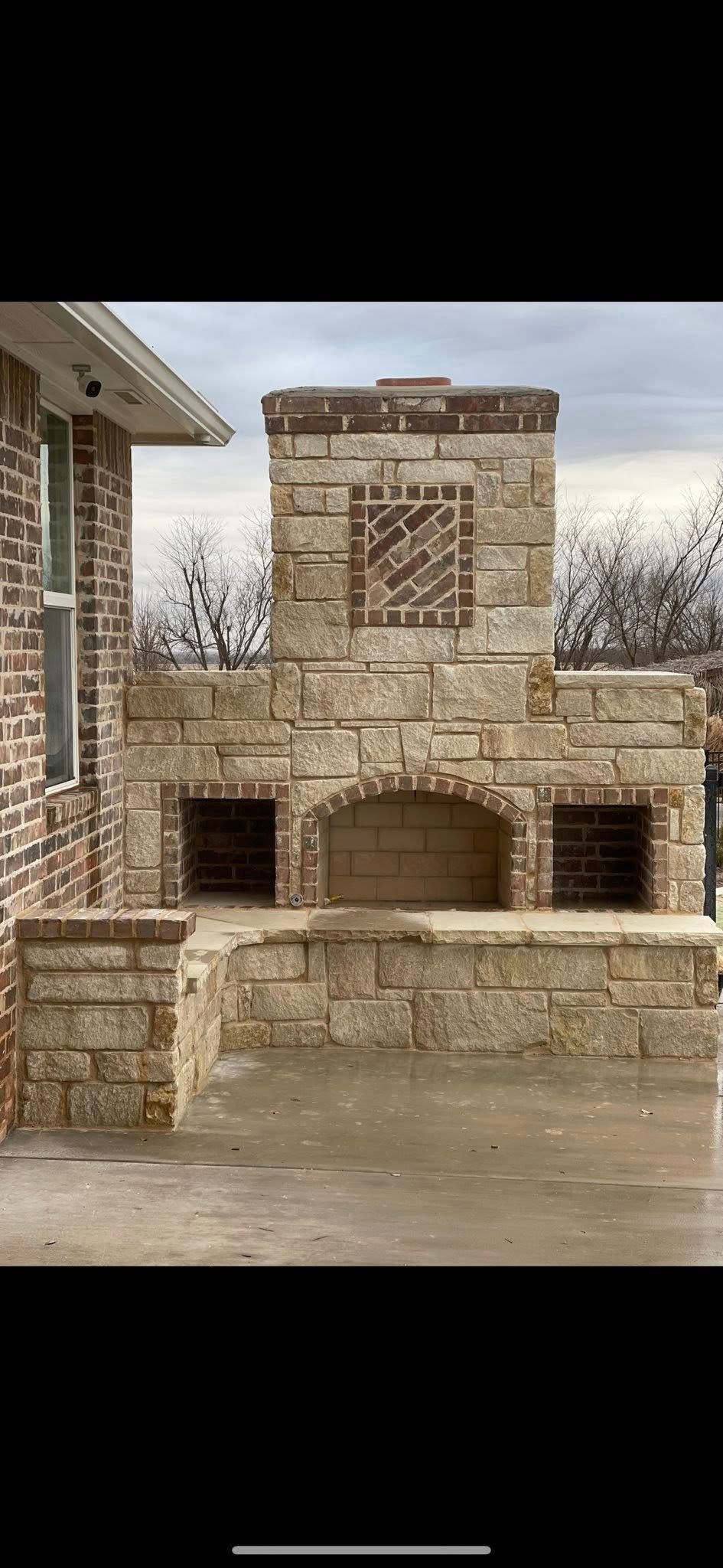 Stone outdoor fireplace and chimney built into a patio wall under an overcast sky