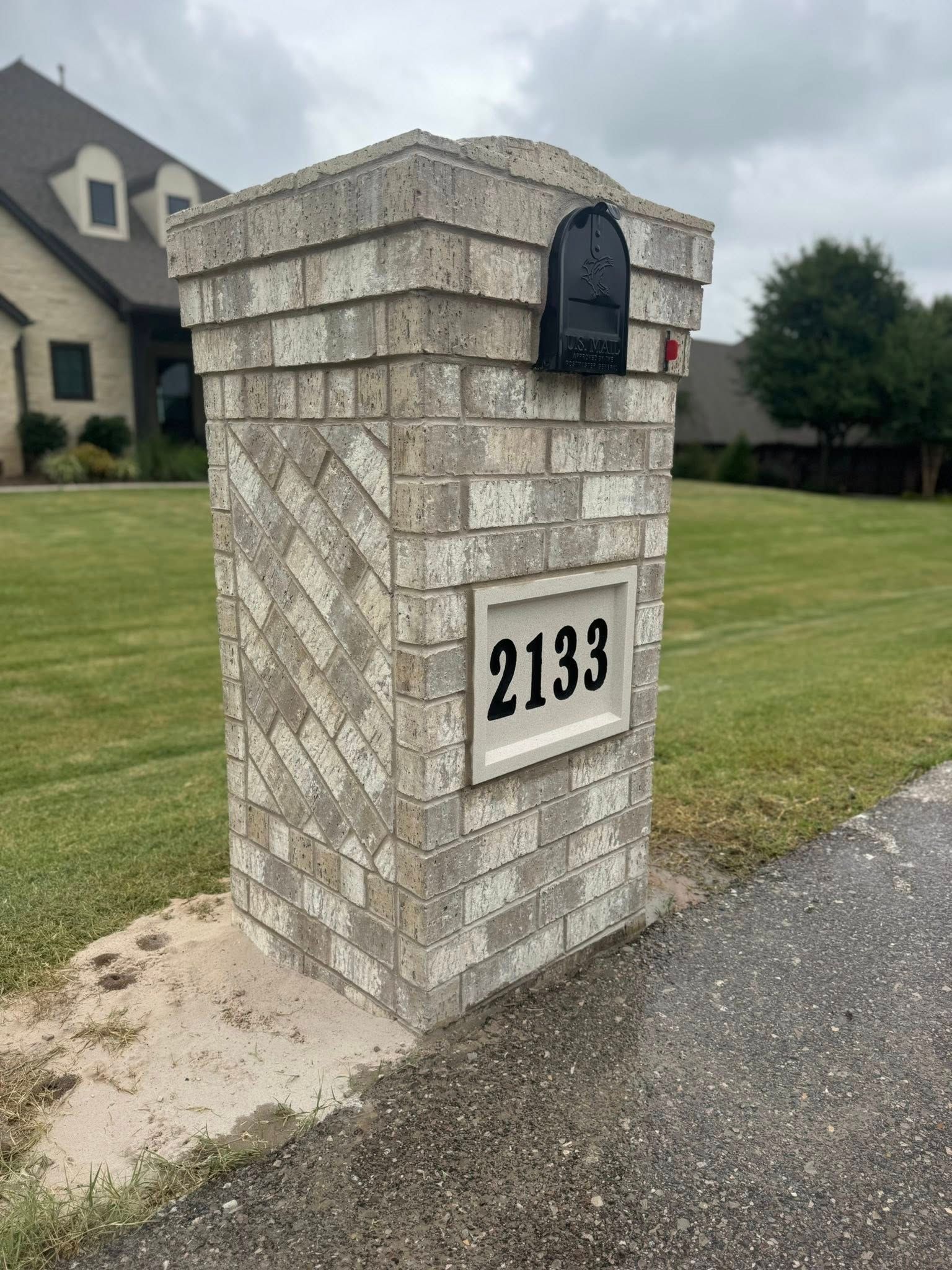 Stone mailbox with house number 2133 beside a driveway on a suburban lawn