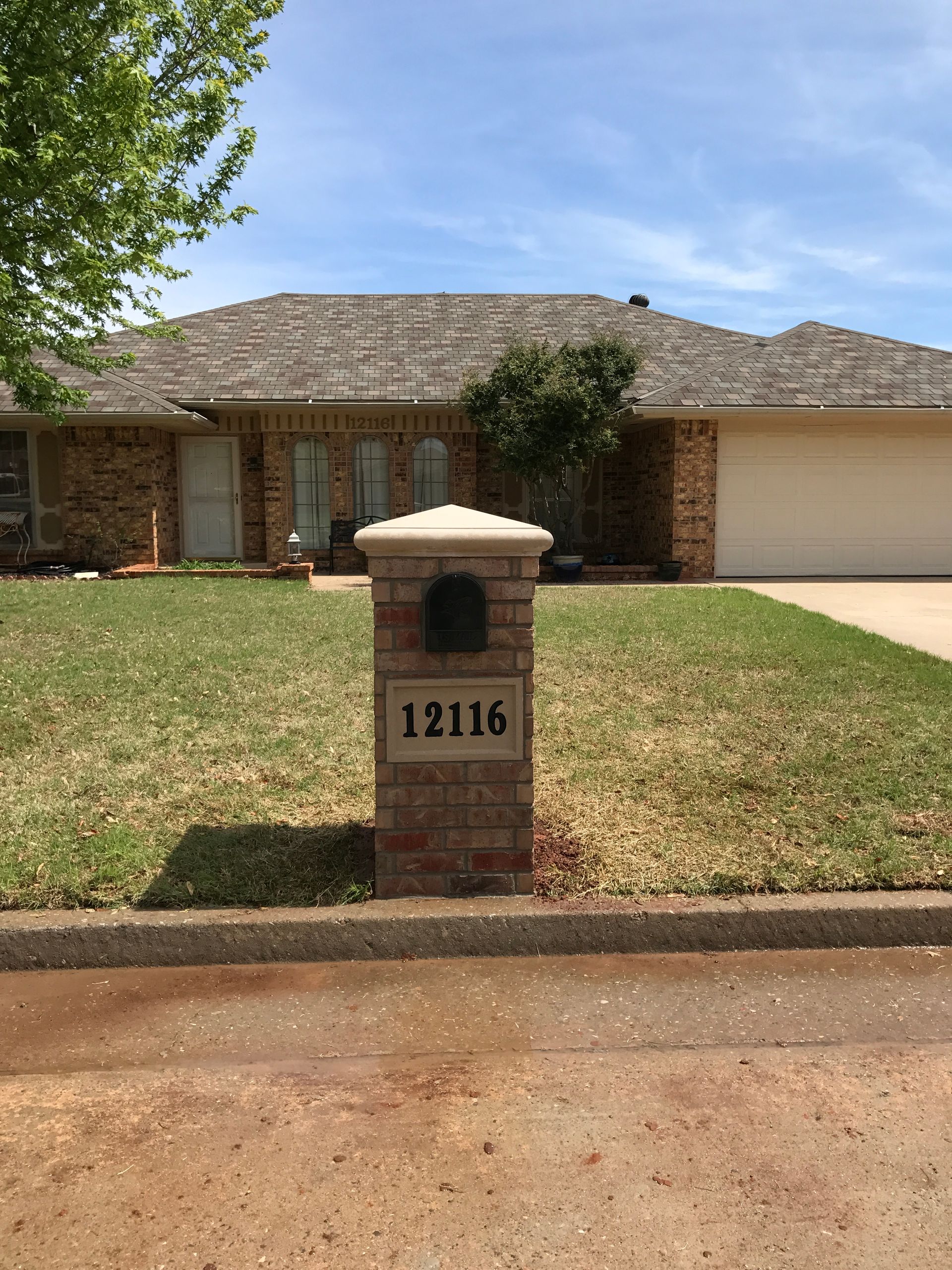 Brick house with a tiled roof and front mailbox reading 12116 along a quiet street.