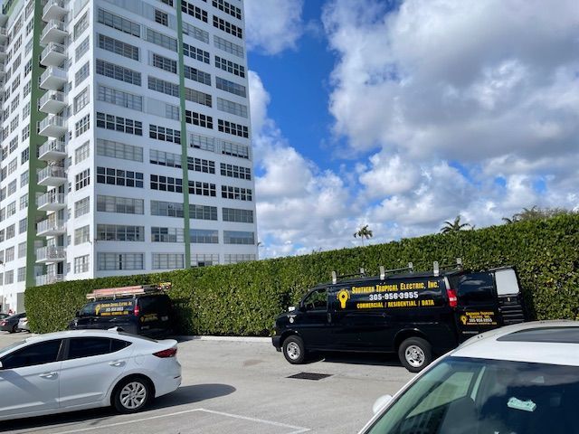 Two black vans with company logos parked in front of a tall building on a sunny day.