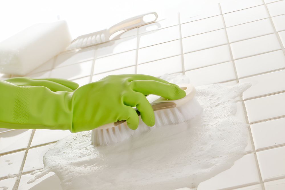 A Person Wearing Green Gloves Is Cleaning A Tile Floor With A Brush — Crystal Clear In Guyra, NSW