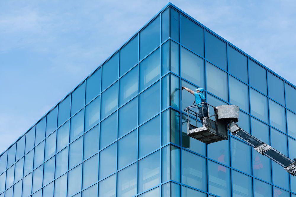 A Man Is Cleaning The Windows Of A Tall Building — Crystal Clear In Armidale, NSW