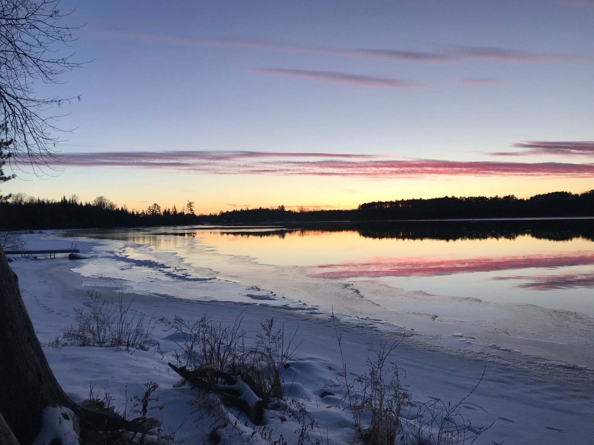A sunset over a lake with snow on the shore