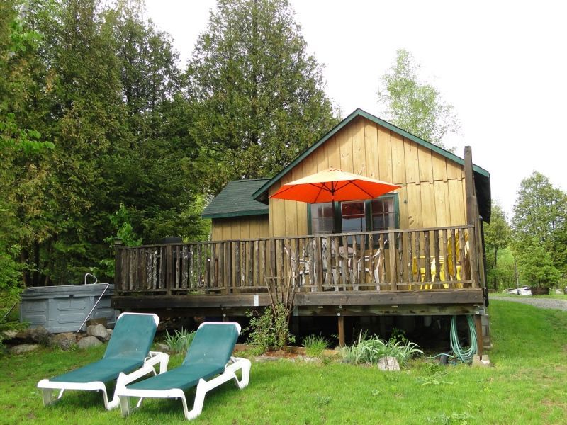 Two lounge chairs are in front of a cabin with an orange umbrella