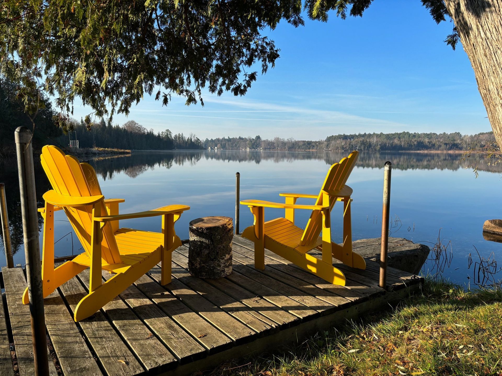 Two yellow adirondack chairs on a dock overlooking a lake