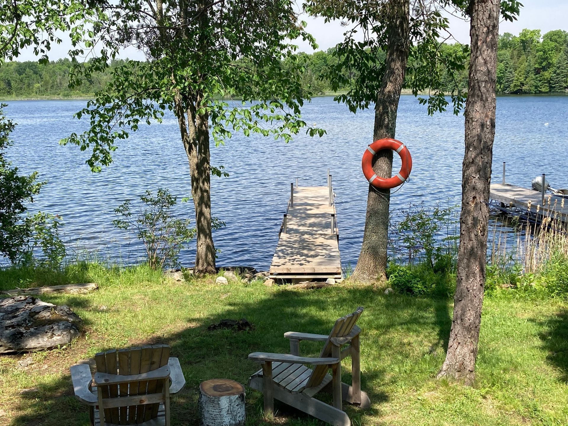 A lake with a dock and chairs in the foreground and trees in the background.