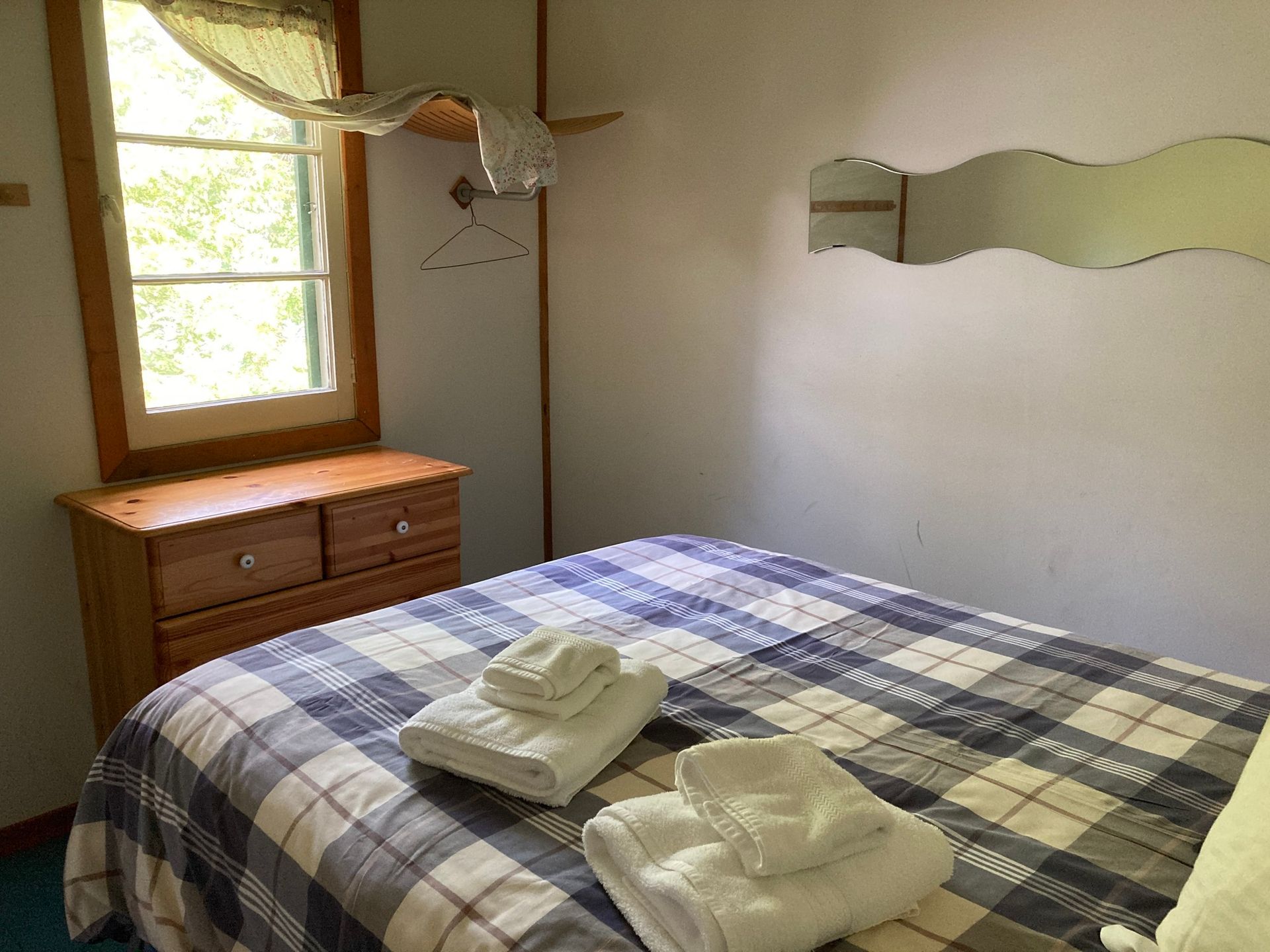 A bedroom with a bed , dresser , mirror and window.