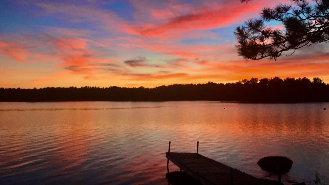 A sunset over a lake with a dock in the foreground.