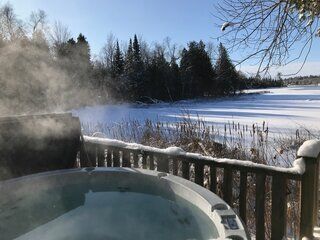A hot tub on a deck with a view of a snowy field.