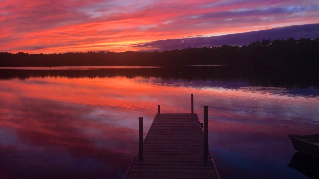 There is a dock in the middle of a lake at sunset.